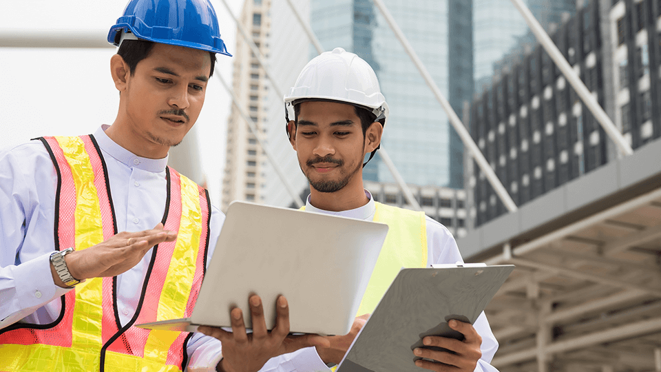作業着とヘルメットを着用している外国人技術者2人が業務について相談している様子の画像