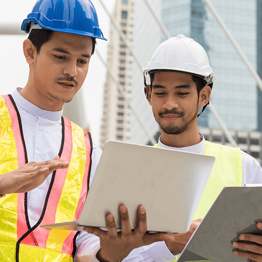 作業着とヘルメットを着用している外国人技術者2人が業務について相談している様子の画像